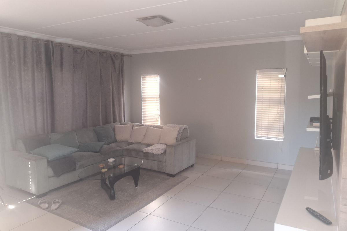 A living room featuring neutral tiled flooring, coved ceilings, and natural light filtered through venetian blinds.