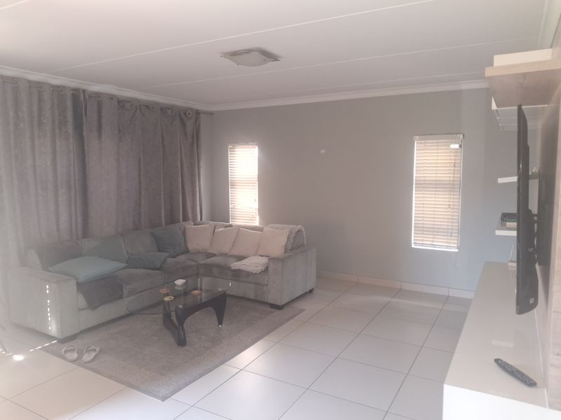 A living room featuring neutral tiled flooring, coved ceilings, and natural light filtered through venetian blinds.
