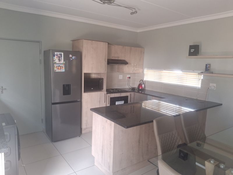 A functional kitchen featuring light wood-finish cabinetry, dark granite countertops, integrated appliances, and tiled flooring, offering a clean and practical cooking space.