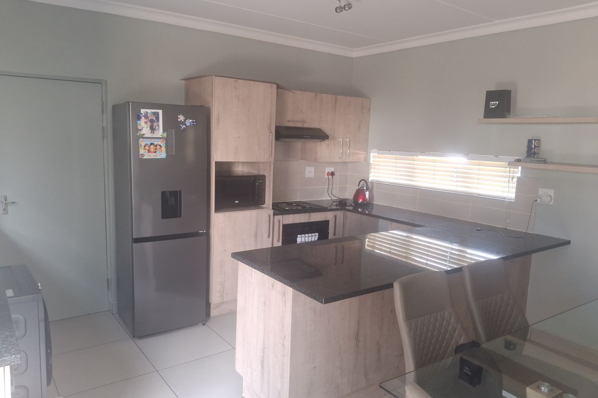 A functional kitchen featuring light wood-finish cabinetry, dark granite countertops, integrated appliances, and tiled flooring, offering a clean and practical cooking space.