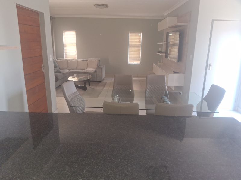 Open-plan living and dining area featuring tiled flooring, a granite kitchen countertop, and a built-in media unit.