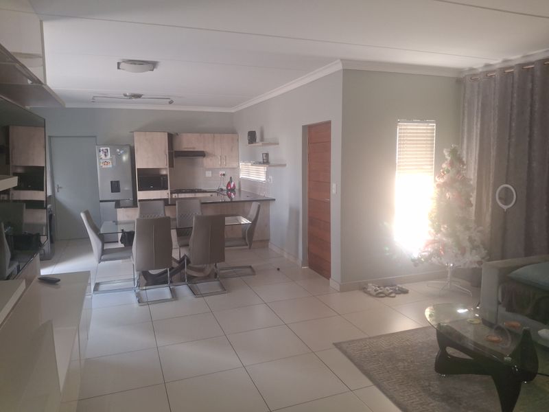 An open-plan living and dining area featuring tiled floors, a modern kitchen with built-in cabinetry, and a breakfast bar.