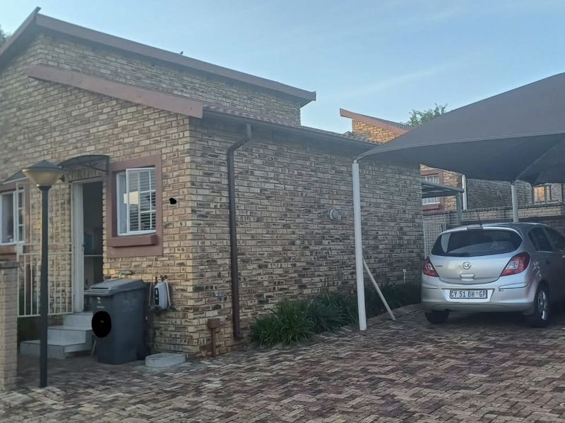 Front exterior view of a face brick townhouse featuring a paved driveway and a shade cloth carport for vehicle parking.