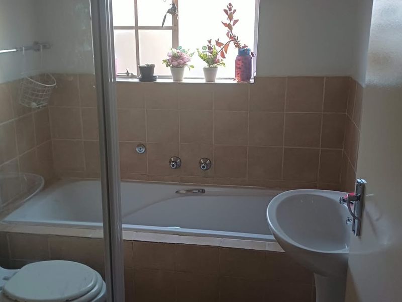A functional bathroom featuring a built-in bathtub with tiled surround, a pedestal sink, and a toilet, offering a practical layout for daily use.