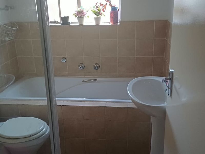 A functional bathroom featuring a built-in bathtub, pedestal basin, and toilet with neutral tiled finishes.