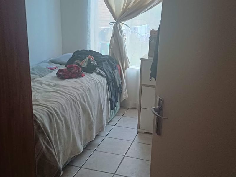 A compact bedroom featuring tiled flooring and a window, viewed from the doorway.
