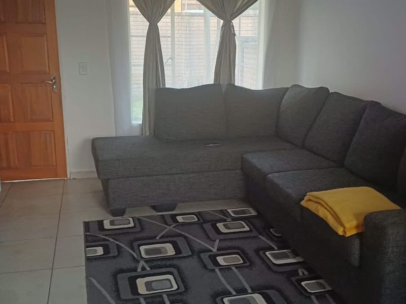A functional living room featuring tiled flooring, a timber entrance door, and a large window providing natural light.