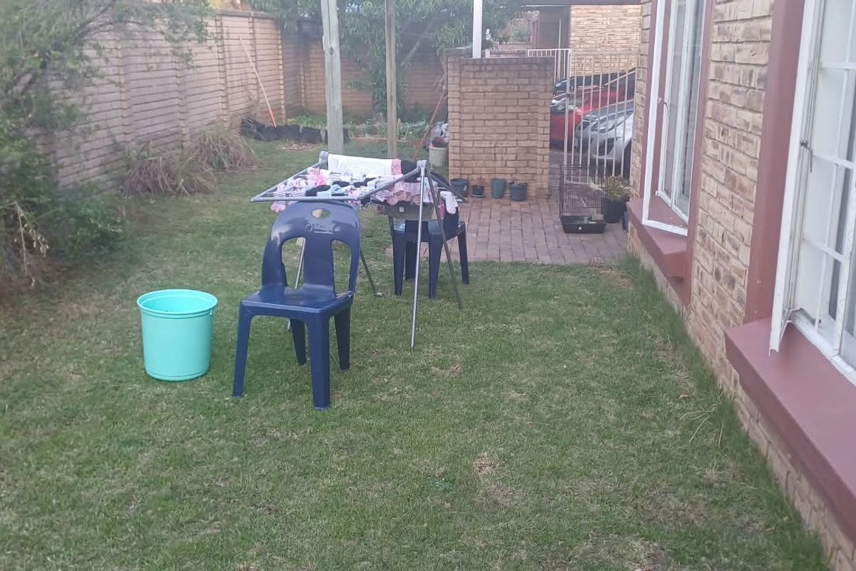 A rear garden area featuring a lawn, brick boundary wall, and a paved section leading to the side of the townhouse.