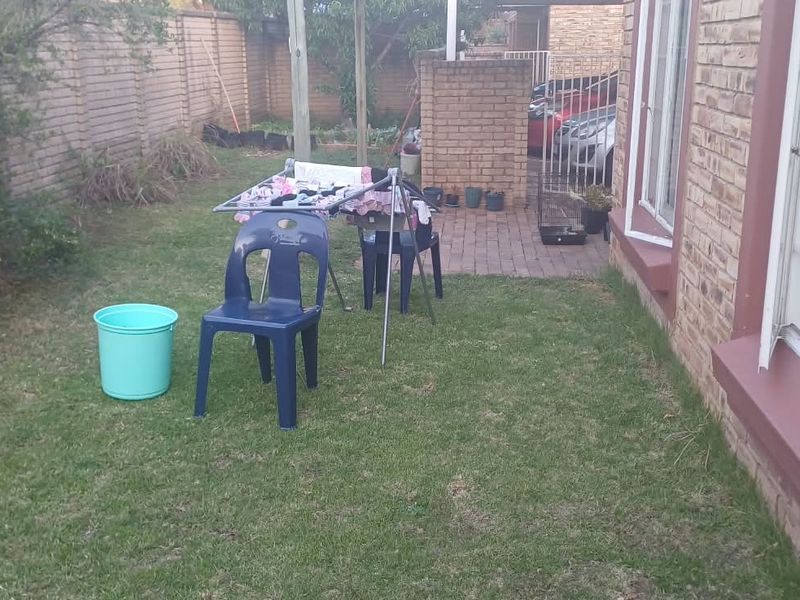 A rear garden area featuring a lawn, brick boundary wall, and a paved section leading to the side of the townhouse.