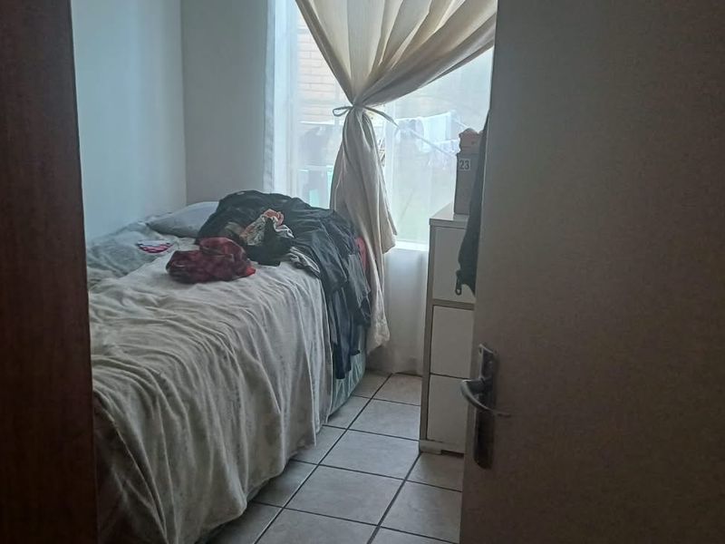 A compact bedroom featuring tiled flooring and a window with curtain rails, offering a functional space for a single bed.
