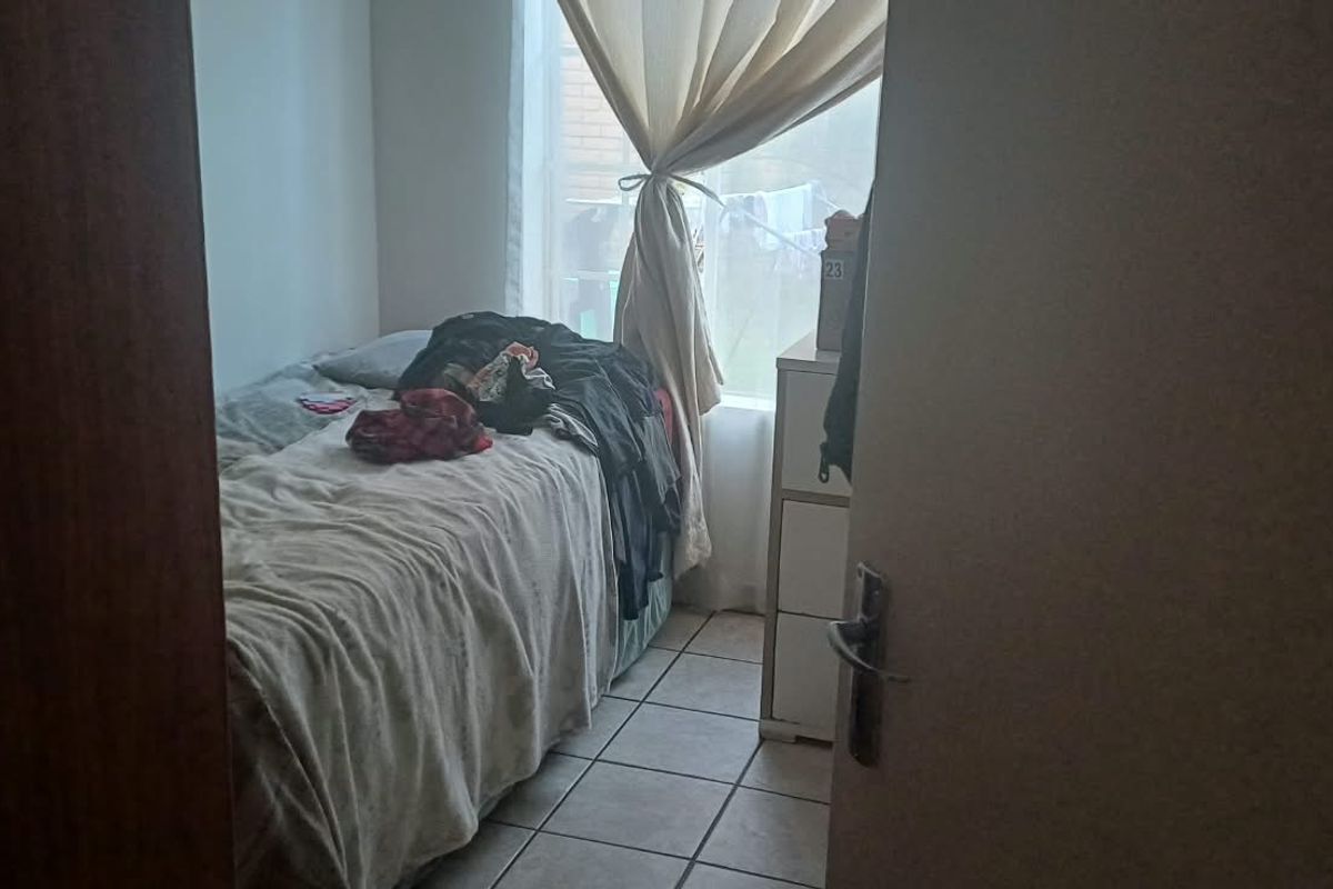 A compact bedroom featuring tiled flooring and a window with curtain rails, offering a functional space for a single bed.