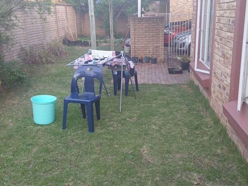 A rear garden area featuring a small paved patio, brick boundary walls, and access to the home via sliding glass doors.