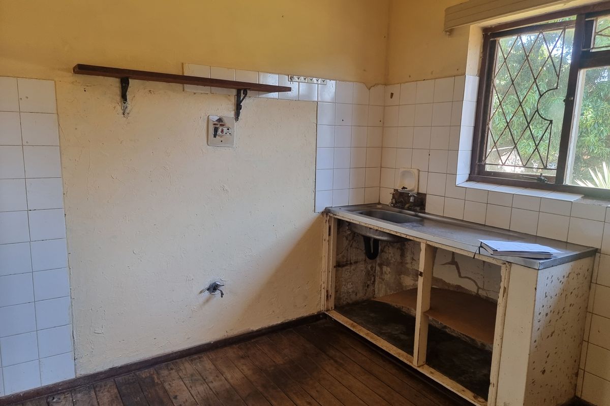 A dated kitchen area featuring a stainless steel sink, tiled splashback, and timber flooring, currently requiring significant renovation and cabinetry repairs.