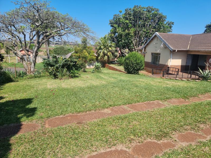 A spacious rear garden featuring a well-maintained lawn, mature trees, and a paved patio area adjacent to the house.