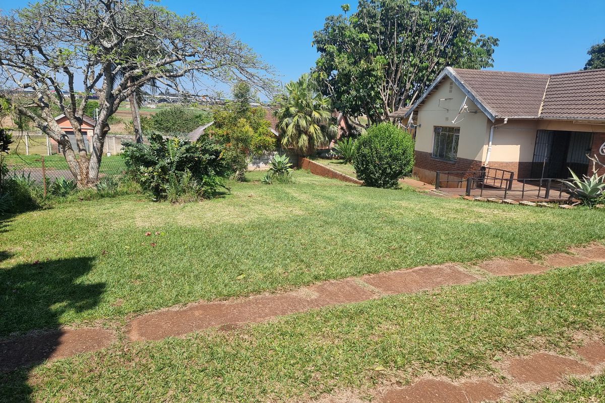 A spacious rear garden featuring a well-maintained lawn, mature trees, and a paved patio area adjacent to the house.