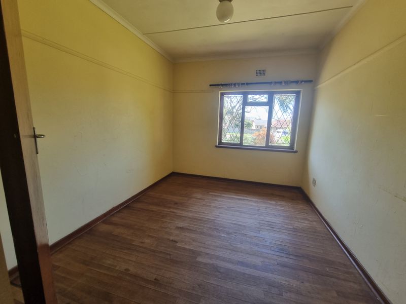 An empty bedroom featuring original wooden flooring, security bars on the window, and classic picture rails, offering a blank canvas for renovation.