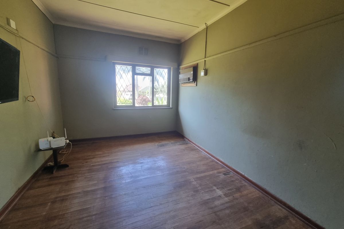 An empty living room featuring original wooden flooring, a leaded glass window, and a wall-mounted air conditioning unit.