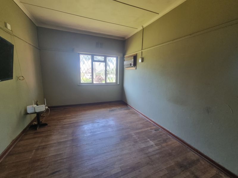 An empty living room featuring original wooden flooring, a leaded glass window, and a wall-mounted air conditioning unit.