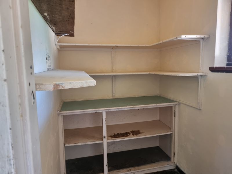 A small, dated scullery or pantry area featuring built-in shelving and cabinetry, requiring cosmetic updates and refurbishment of the interior finishes.