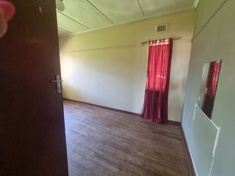 An empty bedroom featuring laminate flooring and a ventilation grille, requiring cosmetic updates to the wall finishes.