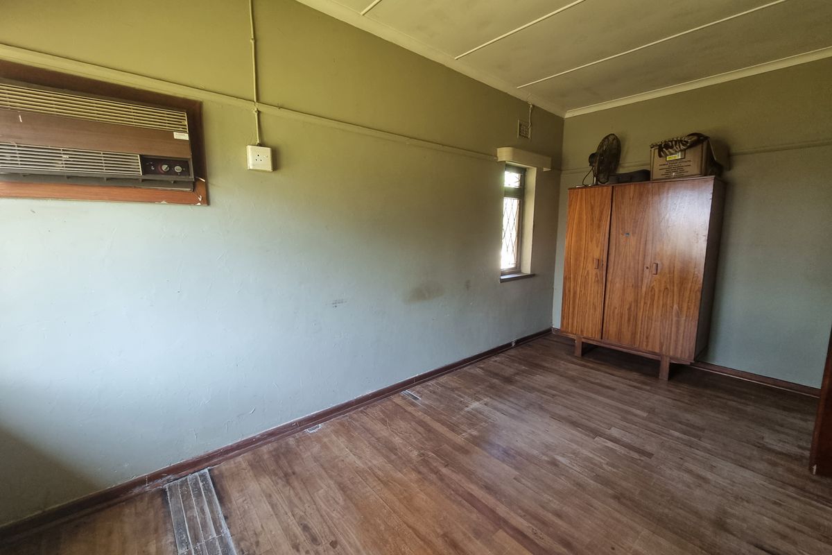 A bedroom featuring timber flooring, a wall-mounted air conditioning unit, and a window, presenting a blank canvas for renovation or restyling.