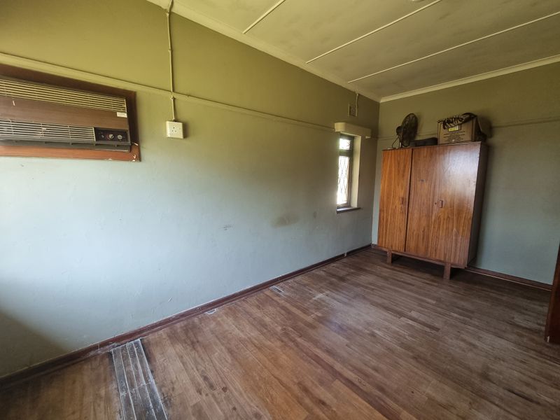 A bedroom featuring timber flooring, a wall-mounted air conditioning unit, and a window, presenting a blank canvas for renovation or restyling.