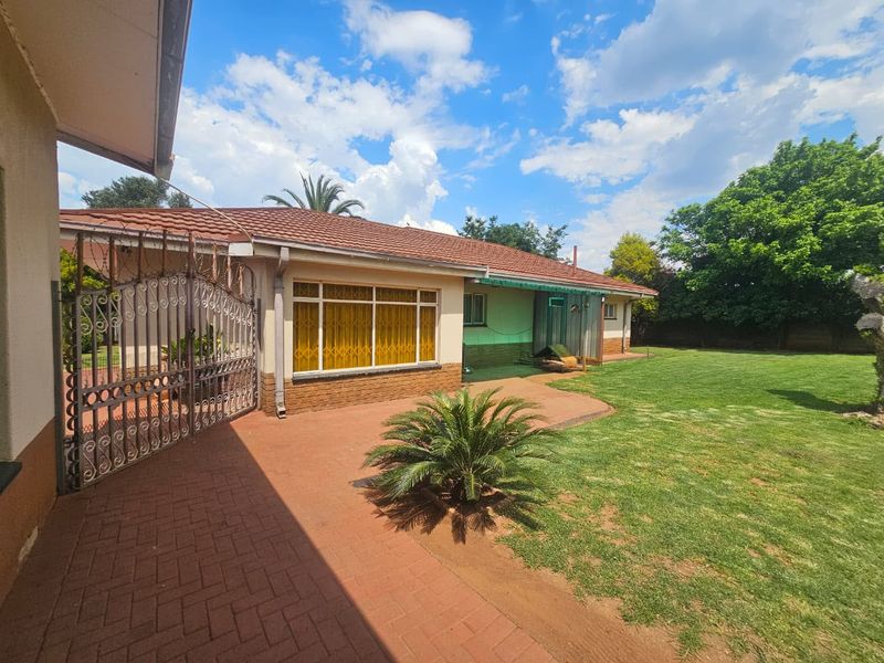 Rear view of the property featuring a paved patio area, lawn, and secure metal gate access to the side of the house.