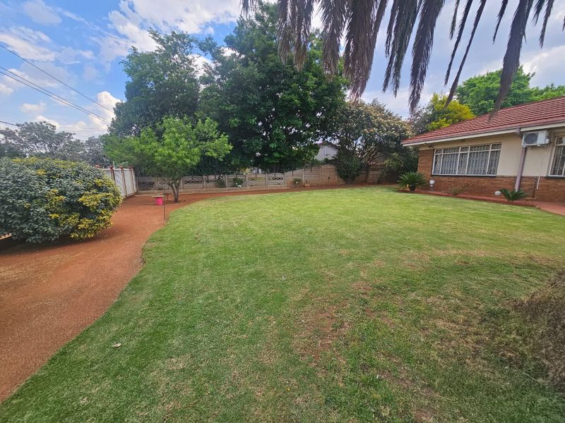 A well-maintained residential garden featuring a spacious lawn, mature trees, and perimeter boundary walls.