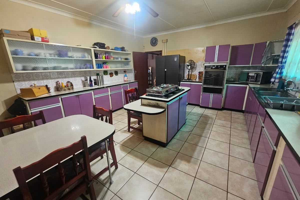 Spacious kitchen featuring extensive built-in cabinetry, a central island with cooktop, built-in oven, and tiled flooring, offering significant potential for modern renovation.