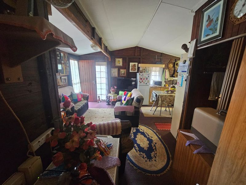 Open plan living and kitchen area featuring rustic timber wall paneling and exposed ceiling beams, offering a cozy, traditional cabin-style atmosphere.