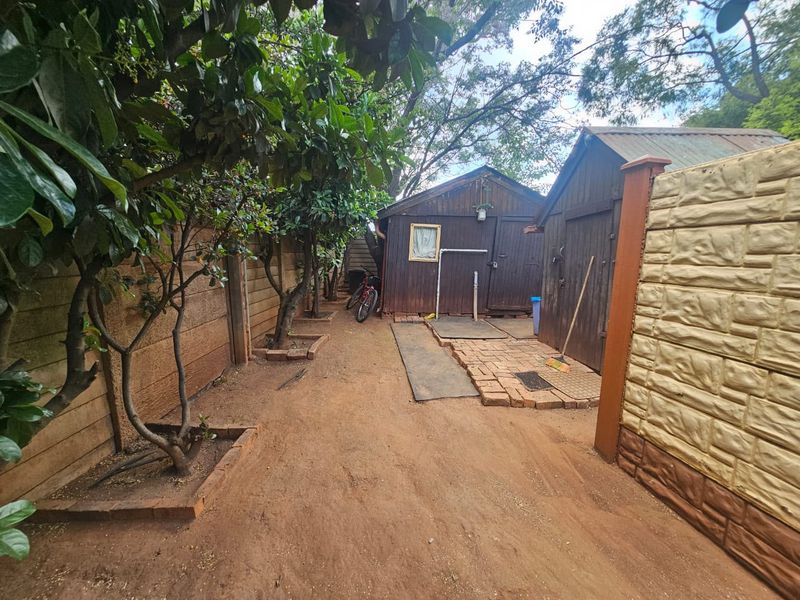 Rear garden area featuring timber storage sheds, brick paving, and perimeter precast concrete walling with mature trees.