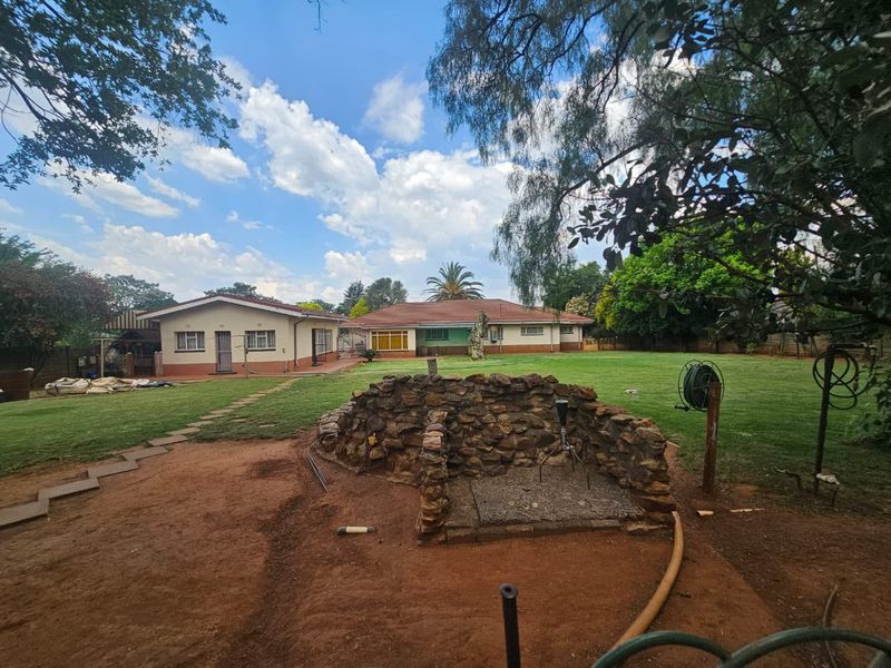 Spacious rear garden featuring a stone-clad fire pit, expansive lawn, and paved pathways leading to the main residence.