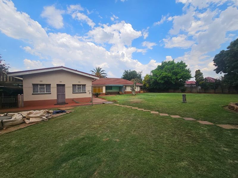 Spacious rear garden featuring a well-maintained lawn, paved pathway, and the rear elevation of the house with security-fitted windows.