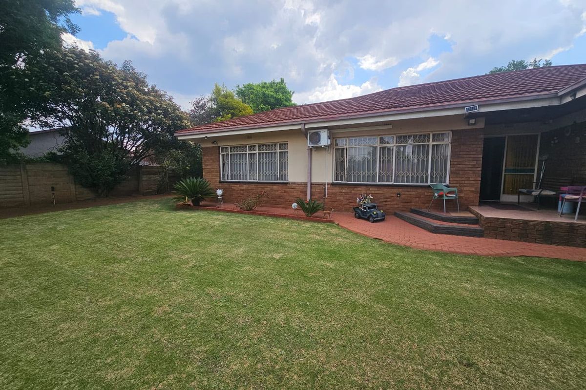Rear view of the house featuring a brick facade, tiled roof, security bars on windows, an air conditioning unit, and a paved patio area.