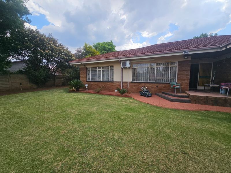 Rear view of the house featuring a brick facade, tiled roof, security bars on windows, an air conditioning unit, and a paved patio area.