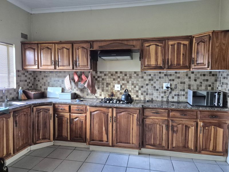A functional kitchen featuring traditional wooden cabinetry, granite countertops, a mosaic tile backsplash, and a gas hob with an integrated extractor fan.