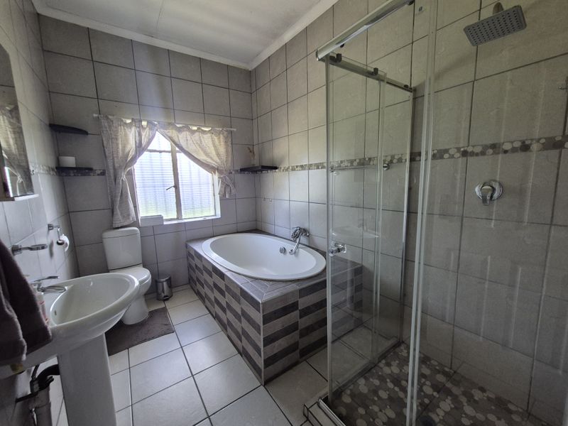 A functional bathroom featuring a pedestal basin, toilet, built-in bathtub, and a separate glass-enclosed shower with a rainfall shower head.
