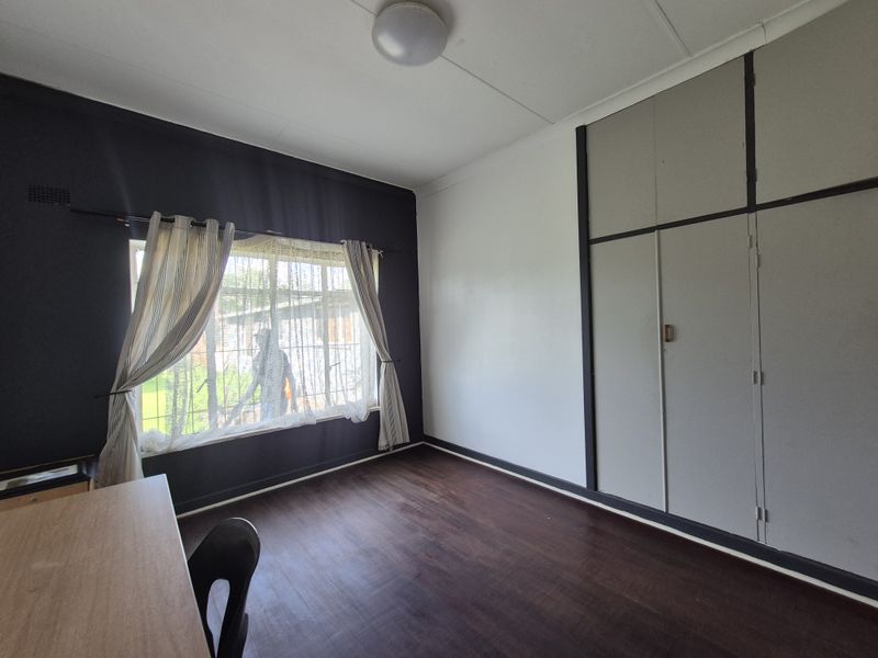 A bedroom featuring built-in cupboards, laminate flooring, and a window with security bars, offering a functional space ready for personalization.