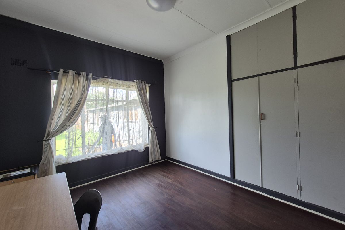 A bedroom featuring built-in cupboards, laminate flooring, and a window with security bars, offering a functional space ready for personalization.