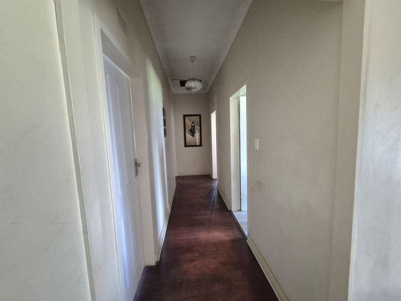 A functional hallway featuring hardwood flooring and access to multiple rooms, showing signs of wear on the wall finishes.