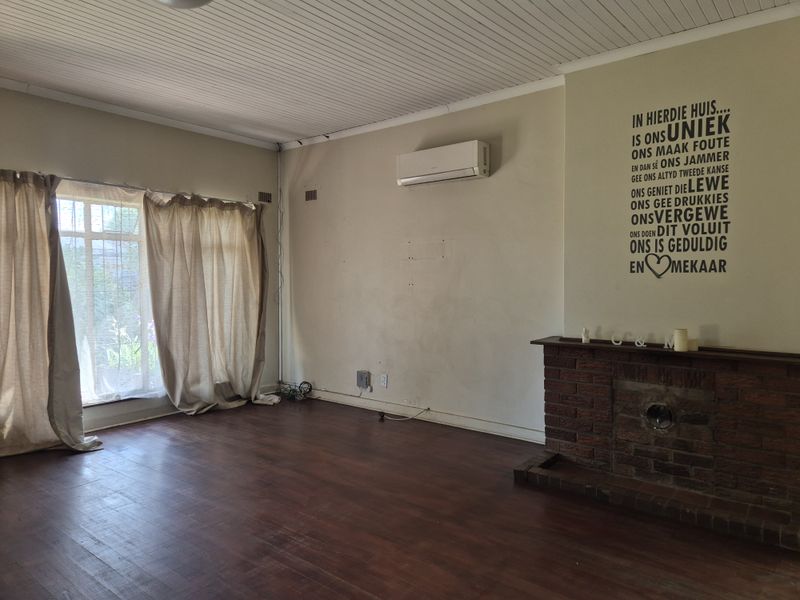 Spacious living room featuring a classic brick fireplace, timber flooring, and a wall-mounted air conditioning unit.