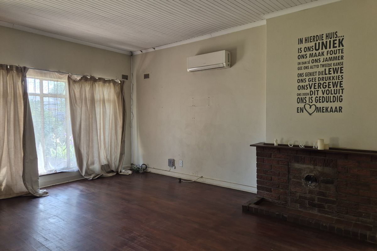 Spacious living room featuring a classic brick fireplace, timber flooring, and a wall-mounted air conditioning unit.