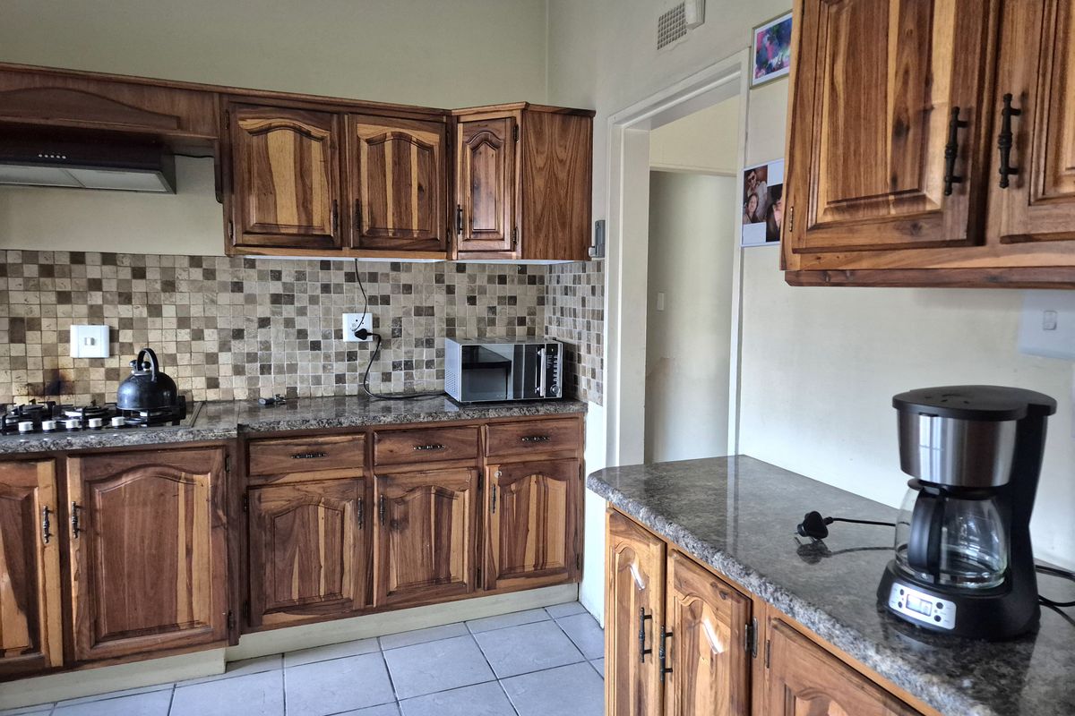 A functional kitchen featuring warm-toned wooden cabinetry, granite countertops, and a mosaic tile backsplash, providing ample storage and workspace.