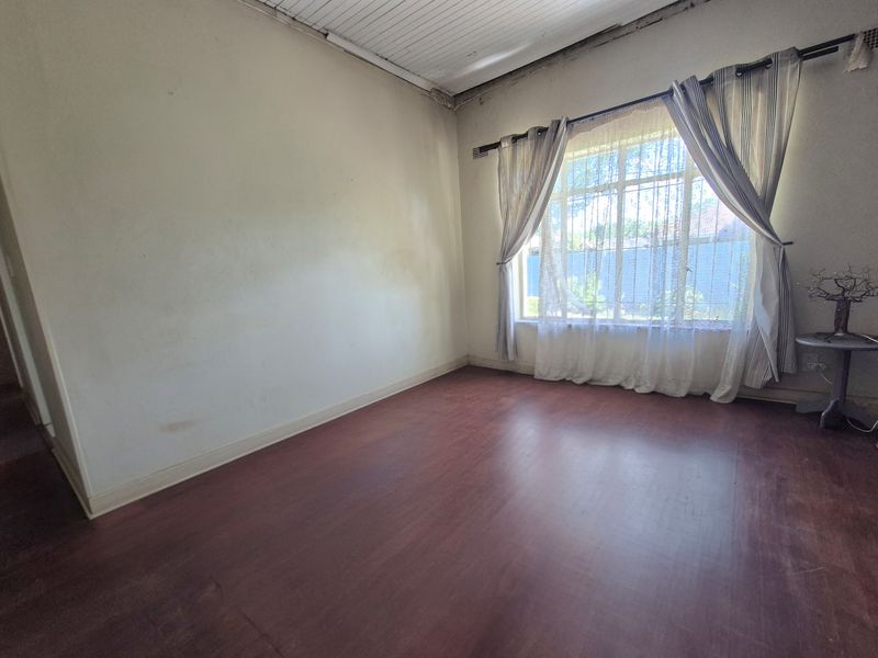 An empty living room featuring timber flooring and a large window, requiring cosmetic updates to the walls and ceiling.