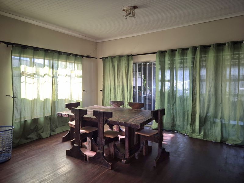 Dining room featuring timber flooring and beadboard ceiling, with visible wall cracks requiring attention. Large windows provide natural light.
