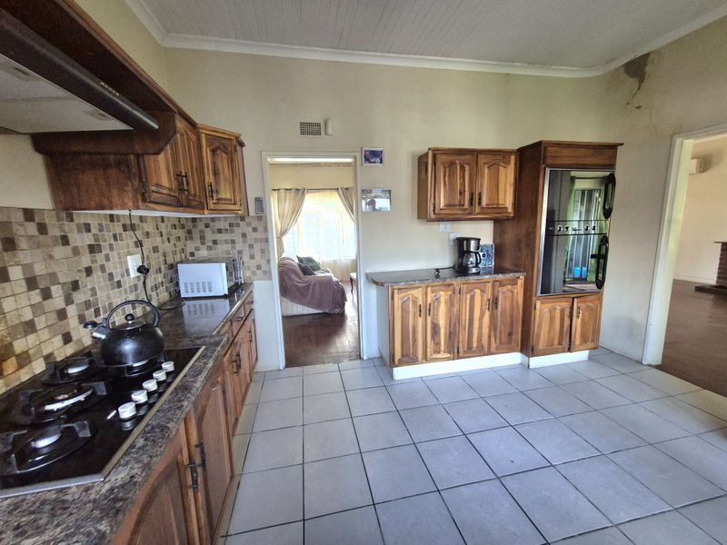 A dated kitchen featuring wooden cabinetry, granite countertops, a gas hob, and built-in oven, with visible wall damage near the doorway.
