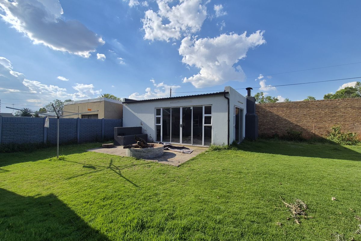 Rear view of the property featuring a spacious lawn, a concrete patio with a built-in fire pit, and sliding glass doors leading into the home.
