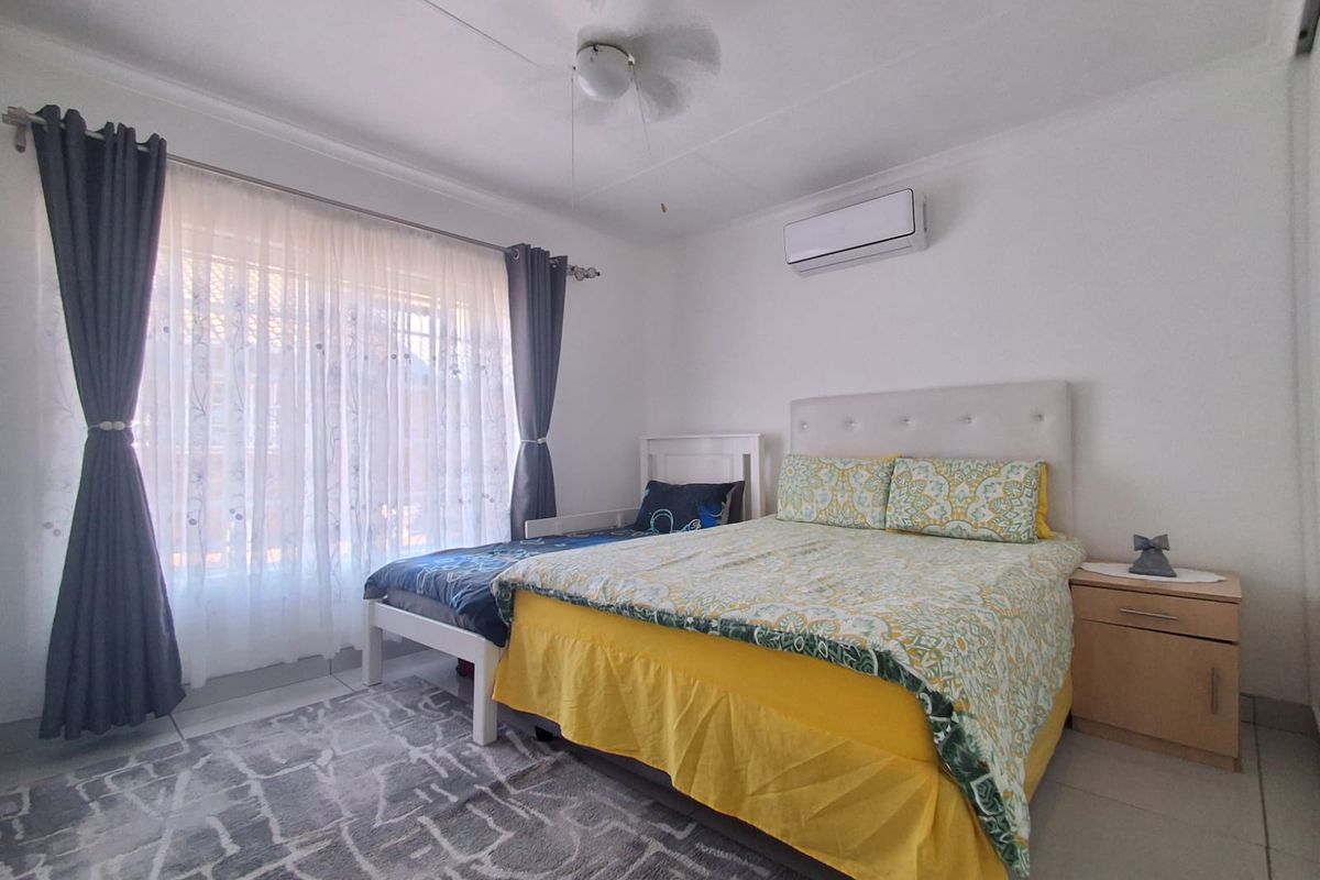 A well-maintained bedroom featuring tiled flooring, a ceiling fan, and a wall-mounted split-system air conditioner for climate control.
