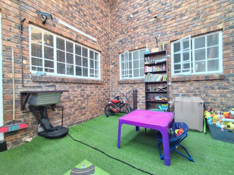 A private rear courtyard featuring face brick walls, steel-framed windows, and a functional utility sink area with artificial grass flooring.