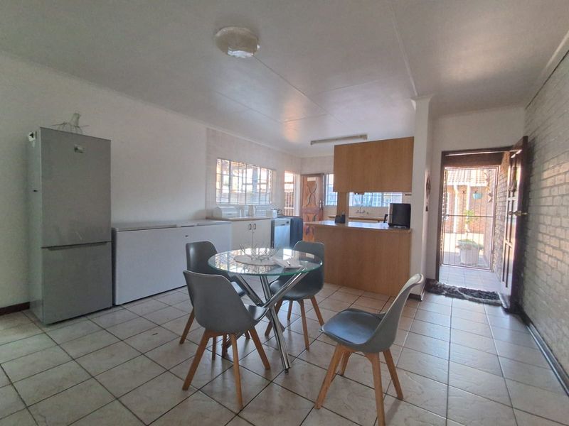 Open-plan kitchen and dining area featuring tiled flooring, wooden cabinetry, and a breakfast bar, with direct access to an exterior courtyard.